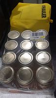 Top view of 12 glass canning jars arranged in a packaging tray, showing metal lids and the plastic wrapping.