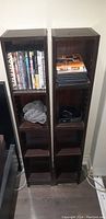 Photo showing two tall dark wood DVD shelving units side by side with DVDs and folded clothes on the shelves.