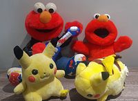 Four stuffed plush toys: two Elmos and two Pikachus grouped together on floor