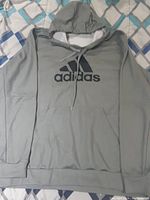 Front view of gray Adidas hoodie with logo, hood with drawstrings, and kangaroo pocket