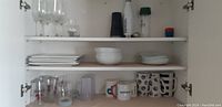 Full cupboard view with glasses on top shelf, plates and bowls on middle shelf, mugs and glasses on bottom shelf.