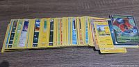A spread of the face of Pokémon cards showing various card types including Energy cards, Trainer cards, and different Pokémon cards laid out flat on a wood surface.