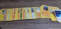 Top-down view of Pokémon cards spread out on a wood surface showing various types with yellow edges.
