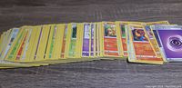 Stack of yellow-bordered Pokemon trading cards laid out flat on a wooden surface