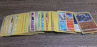 Wide view of a stacked group of approximately 125-130 Pokemon cards showing assorted card edges and some front visible, including Trainer and Energy cards.