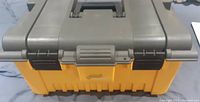 Closed large plastic tool box with yellow bottom and gray lid with handle and black latches.