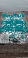 Vacuum sealed transparent plastic bag with teal printed text containing multiple small oxygen absorber packets lying on a wooden surface.