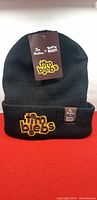 Black knit touque with embroidered 'tim biebs' logo and branded tags against red background.