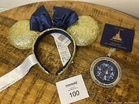 Disney 50th gold sequin Minnie ears headband with navy blue bow and a collectible round ornament with Walt Disney World 50th celebration design on front, all new with tags.