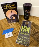 Nightmare Before Christmas notebook, Corkcicle tumbler, and Haunted Mansion door hanger shown together on a wood surface.