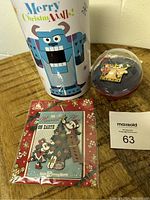 Front view of the holiday-themed tin container featuring Sulley from Monsters Inc, the sealed Disney holiday pin set showing Mickey and Minnie Mouse, and the surprise pin magnet in its plastic capsule.