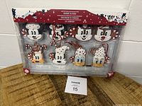 Full packaged set of 8 Disney character Christmas ornaments with candy cane and peppermint designs, new in box on a wooden surface.