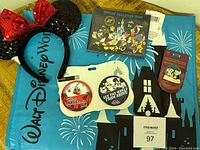 Photo of the entire lot with the Disney World blue bag as background, showing Minnie Mouse ears, autograph book, two buttons, and Disney pin in packaging.