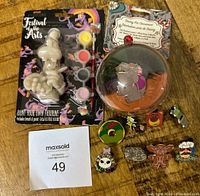 Overall lot with paint your own figurine, pin ornament, and assorted pins displayed on wooden surface with MaxSold lot number.