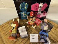 Three Disney Nuimos dolls and two clothing packs displayed on wood with tags attached, labels visible in background
