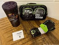 Photo of the black Corkcicle tumbler with purple lid featuring Disney Villains graphics next to the black crossbody bag with front zippered pockets and the adjustable villain-themed strap on wooden table.