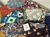 Photo showing multiple LuLaRoe clothing items with Disney character prints, including Mickey and Minnie Mouse, various colors and patterns, folded and stacked on a wooden surface.