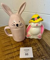 Pink Rae Dunn bunny mug with bunny ears lid and black text 'Bunny Kisses', next to vintage bunny candle with yellow floral hat.