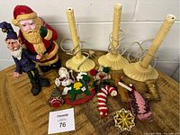 Lot of vintage Christmas decorations including hard plastic Santa Claus and elf figurines, three yellow candleholders, and assorted ornaments on wooden table.