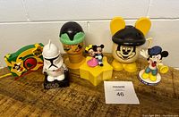 Photo showing the front view of various vintage Disney and Star Wars collectible items on a table including cups, candy dispensers, and figures.