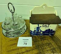 View of vintage ceramic salt cellar with blue windmill design and glass cruet set in metal holder on wooden surface.