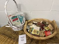 Lot showing two baskets, one filled with vintage matchbooks, other with Singer sewing needles still in packaging.