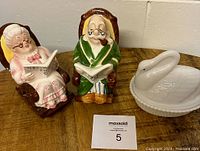 Photo showing the two retirement couple banks and the white milk glass swan bank on a wooden surface.