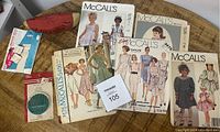 Eight vintage McCall's sewing pattern envelopes mostly for women's and children's dresses, plus sewing accessory packages on a round wooden table.