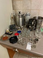 Full lot view showing ice buckets, shot glasses, decanter, ashtrays, jiggers, and accessories.