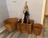 Photo showing all items in the lot: wooden crate holding umbrellas, large wicker basket, and smaller wicker basket.