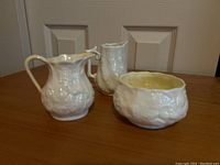 Front view of the three Belleek pieces: two creamers and one sugar bowl on wooden surface.