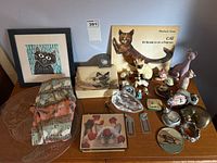 Wide view of all cat-themed collectibles including framed art, book, figurines, glassware, and other small items