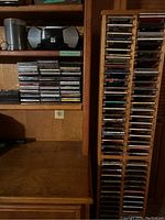 Wide view showing the portable CD player with built-in microphone on wooden shelving alongside stacks of CDs in jewel cases.