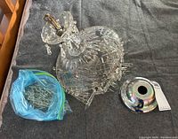 Crystal chandelier laid on fabric surface showing overall shape, cut glass decorative body, hanging crystal prisms, and silver ceiling mount canopy laid next to it.