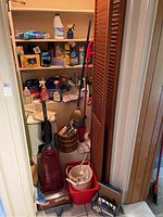 Photo showing the closet with Panasonic upright vacuum, cleaning supplies on shelves, mop, broom, dustpan, buckets, garbage can