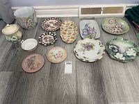 All 12 decorative china items arranged on floor, showing various plates, trivets, and bowls with floral hand-painted designs