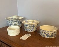 Four ceramic dishes displayed on wooden surface, three with blue floral patterns and lids, one plain white dish.