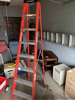 Full view of the 8ft Featherlite aluminum step ladder standing in a garage against a gray wall with various household items around.