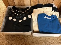 Two boxes with folded cashmere sweaters including a black polka dot cardigan and various cream and blue sweaters.