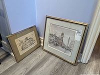 Two framed prints leaning against wall, one larger and one smaller