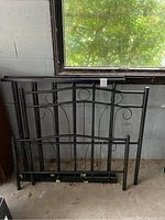 Black metal bed frame components arranged vertically against a wall, showing headboard, footboard, and folding base panels.