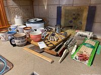 Lot showing an assortment of kitchen items including rice cooker, mugs, cutting boards, and various utensils laid out on kitchen countertop.