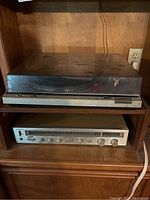 Photo showing Technics turntable model SL-D20 on top shelf with dust cover, and Technics stereo receiver SA-203 on shelf below, both housed in wooden shelved cabinet.