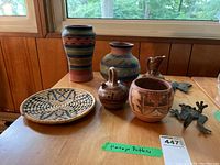 Group photo showing all four Navajo pottery pieces, woven wicker plate, and two metal hangers on wooden table.