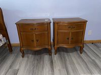 Pair of honey-brown wooden night stands shown from front, each with one drawer and lower cabinet with double doors, surface wear visible.