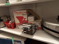 Shelf view showing the Marcato Deluxe pasta machine in front, and the Rigamonti The Master tomato press in the box behind it, also the electric frying pan beside them.