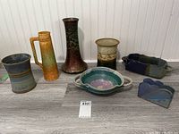 Overview photo showing all pottery pieces together arranged on floor against white paneling. Displays the variety and sizes of the lot.