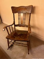 Front view of a solid wood carved rocking chair showing detailed carvings and turned spindles on the backrest and armrests.