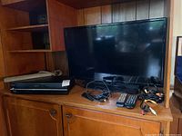 Samsung 32 inch flatscreen TV with remotes and cables placed on wooden furniture along with the Toshiba DVD/VCR player.