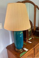 Full view of the blue ceramic lamp with beige pleated fabric shade on wooden surface, showing item's overall height and style.